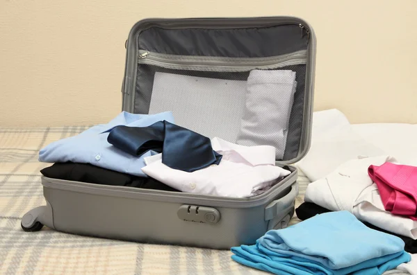 Valise ouverte grise avec vêtements sur le lit — Photo