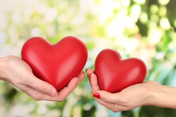 Corazones rojos en las manos de la mujer y del hombre, sobre fondo verde — Foto de Stock