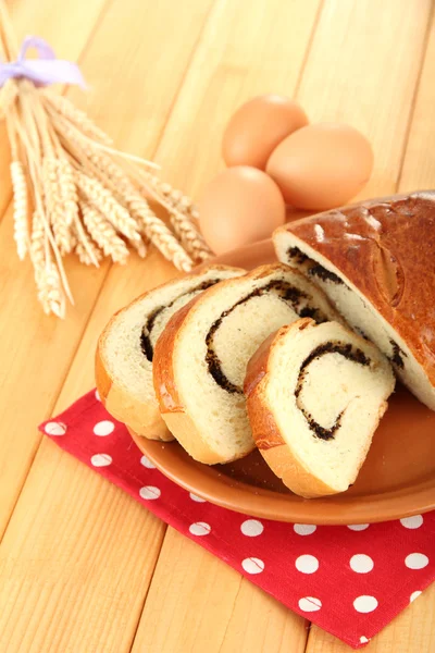 Loaf with poppy seeds on color plate, on wooden background — Stock Photo, Image