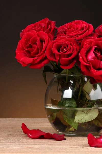 Hermosas rosas rojas en jarrón sobre mesa de madera sobre fondo marrón —  Fotos de Stock