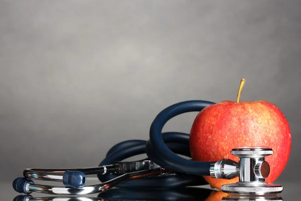 Medical stethoscope and red apple on grey — Stock Photo, Image