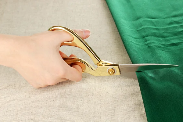 Швея вырезать зеленую ткань на бежевом фоне ткани — стоковое фото