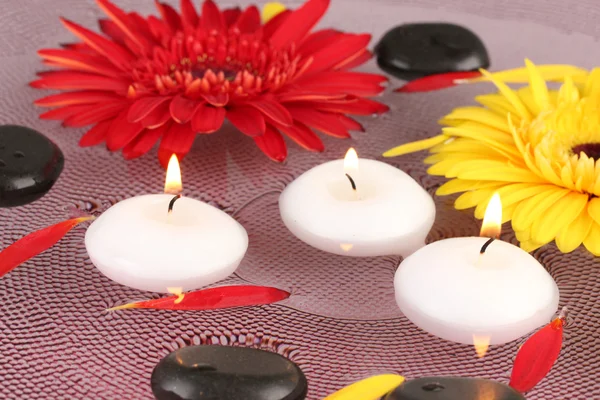 Piedras de spa con flores y velas en agua en el plato —  Fotos de Stock