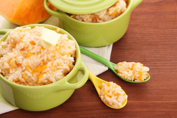 Taste rice porridge with pumpkin in saucepans on wooden background — Stock Photo, Image