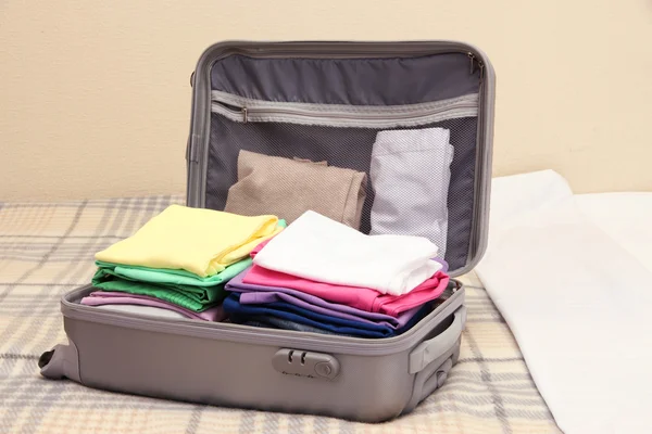 Open grey suitcase with clothing on bed — Stock Photo, Image