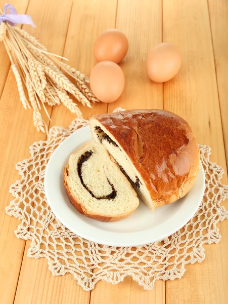 Loaf with poppy seeds on color plate, on wooden background — Stock Photo, Image