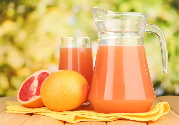 Vaso completo y jarra de zumo de pomelo y pomelos sobre mesa de madera al aire libre —  Fotos de Stock