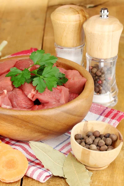Rå nötkött med örter och kryddor på träbord på brun bakgrund — Stockfoto