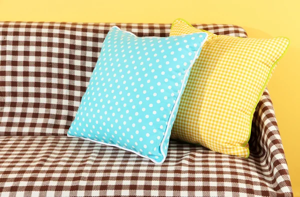 Colorful pillows on couch on yellow background — Stock Photo, Image