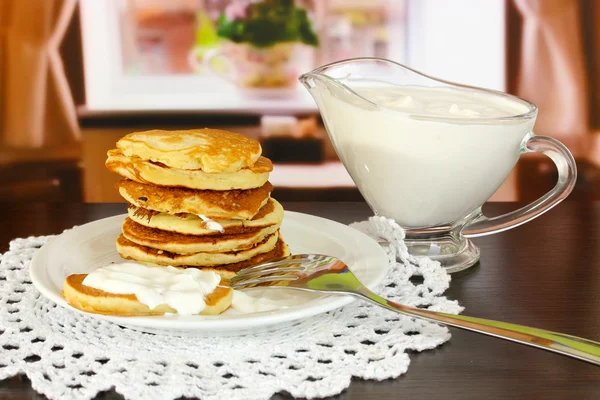 Sweet pancakes on plate with sour cream on table in room — Stock Photo, Image