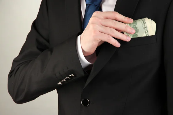 Business man hiding money in pocket on grey background — Stock Photo, Image