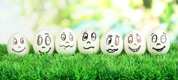 Яйца со смешными лицами на траве на ярком фоне — стоковое фото