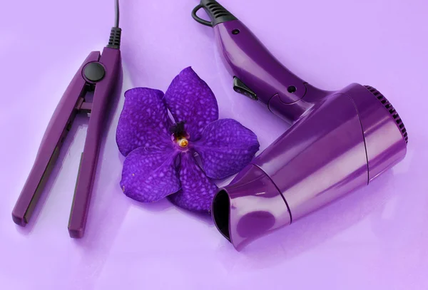 Haartrockner und Glätteisen auf lila Hintergrund — Stockfoto