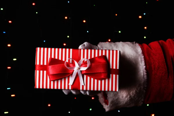 Santa Claus hand holding gift box on bright background — Stock Photo, Image