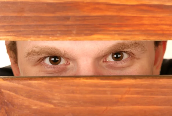 Hombre ojos mirando a través de agujero en escritorio de madera — Foto de Stock