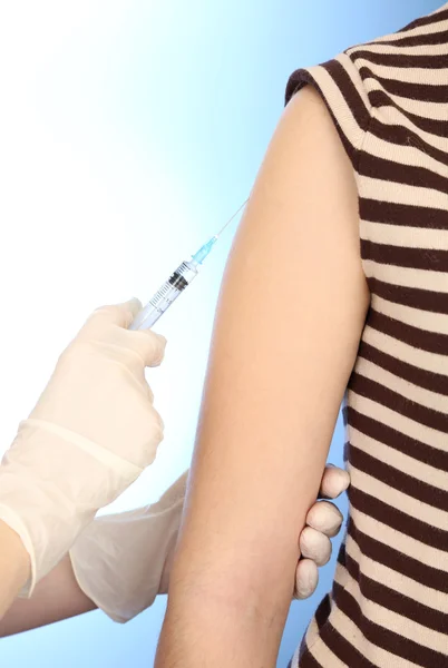 Siringa per medico con vaccino nella spalla del paziente, su sfondo blu — Foto Stock