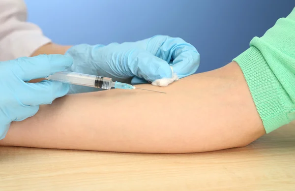 Lekarz gospodarstwa strzykawka szczepionki w strony pacjenta, na niebieskim tle — Zdjęcie stockowe