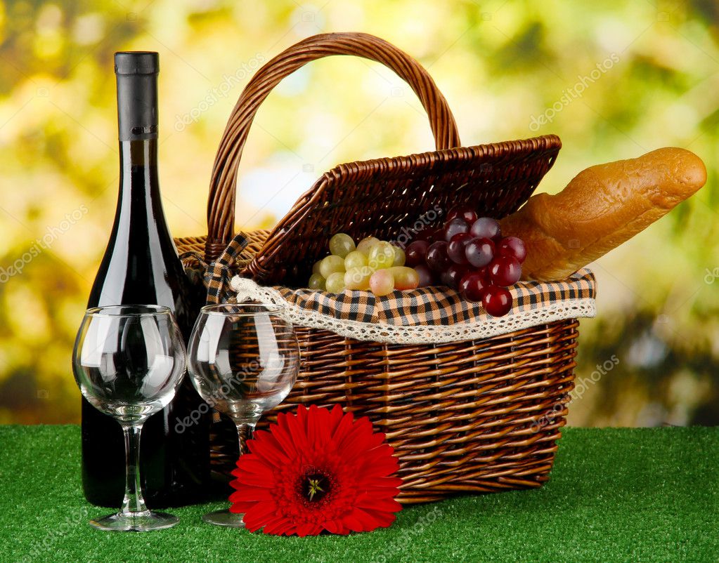 Picnic basket and bottle of wine on grass on bright background — Stock
