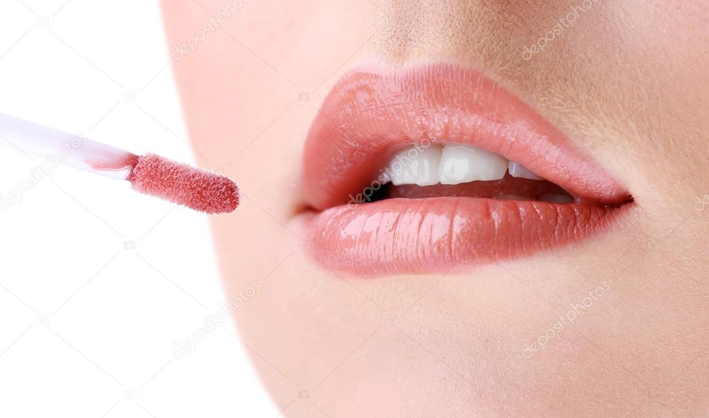 Beautiful young woman applying lip gloss, close up