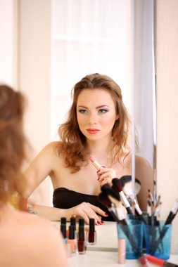 Genç ve güzel bir kadın aynanın yanında makyaj yapıyor.