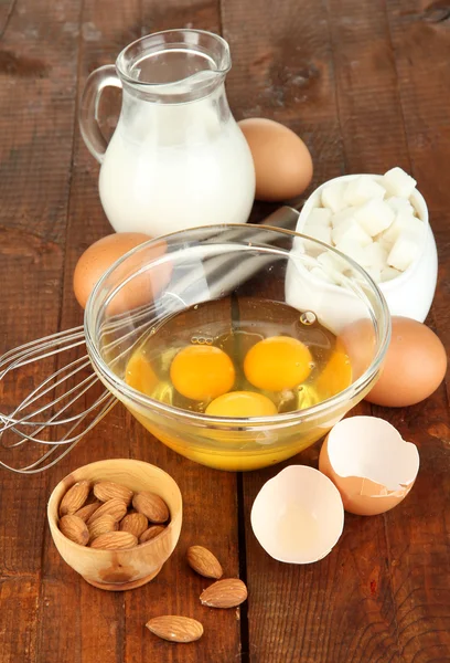 Huevo roto en tazón y varios ingredientes junto a ellos en la mesa de madera de cerca —  Fotos de Stock