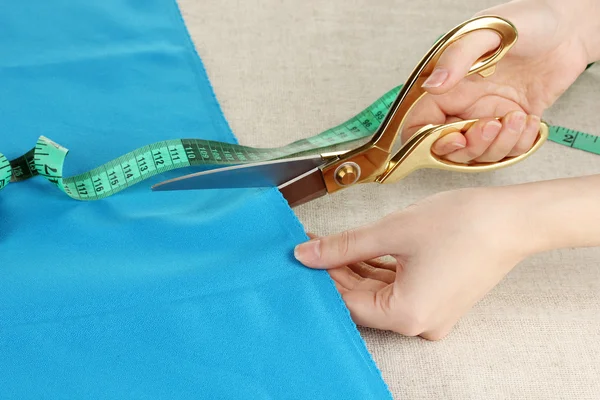 女裁缝师剪蓝色的布米色织物背景上 — 图库照片