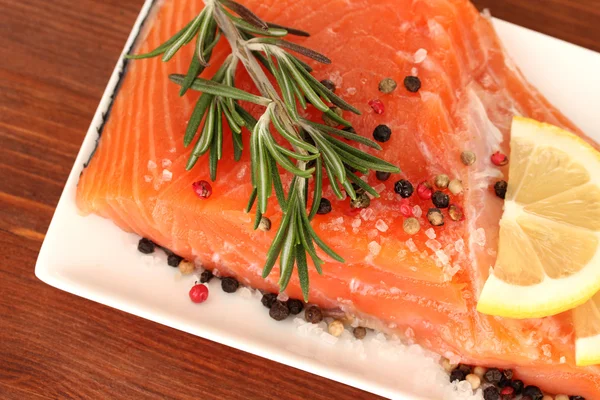 Filete de salmón fresco con hierbas y rodajas de limón en el plato, sobre fondo de madera —  Fotos de Stock