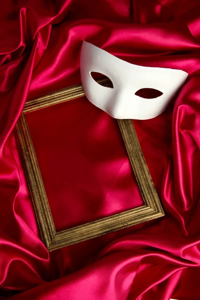 White mask and empty frame on red silk fabric — Stock Photo, Image