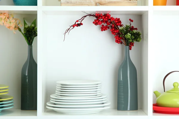 Prateleiras brancas bonitas com utensílios de mesa e decoração — Fotografia de Stock