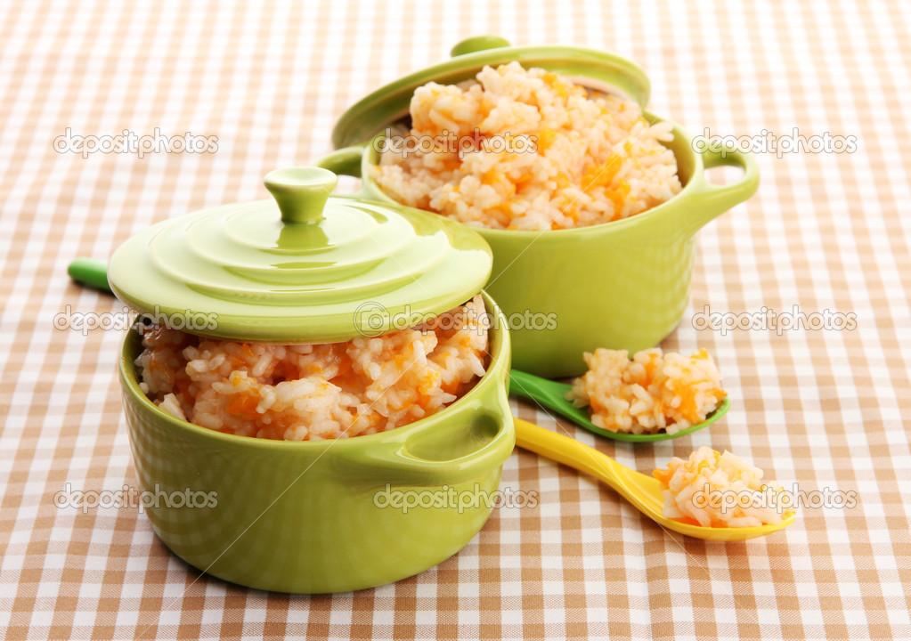 Taste rice porridge with pumpkin in saucepans on tablecloth background