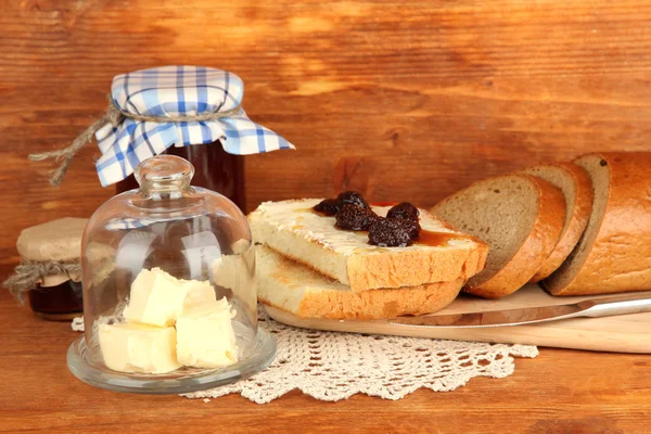 Üveg csészealj üveg fedél és friss kenyeret a vaj, jam, fából készült háttér — Stock Fotó