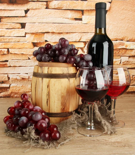 Composition of wine and grapes on wooden barrel on table on brick wall background — Stock Photo, Image