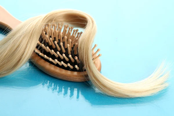 Wooden comb brush with hair, on blue background — Stock Photo, Image