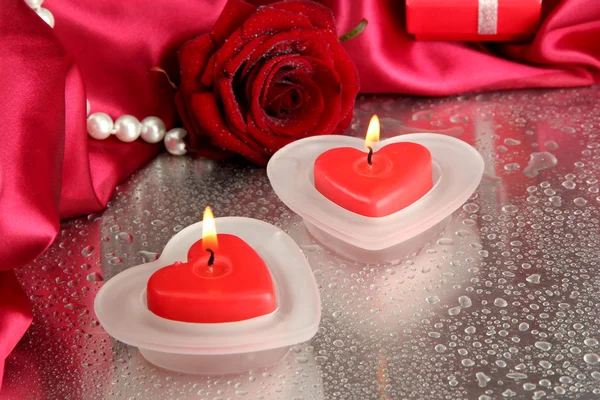 Beautiful candles, rose and red silk on grey wet background — Stock Photo, Image