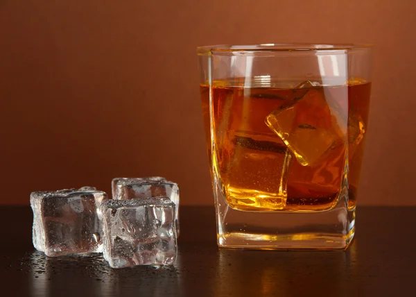 Sklenice whisky a ledu na hnědé pozadí — Stock fotografie