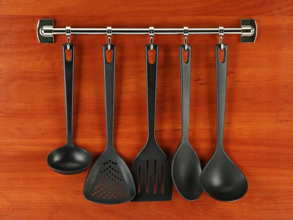 Černá kuchyně nádobí na stříbrné háčky, na dřevěné pozadí — Stock fotografie