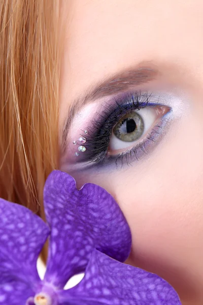 Hermoso ojo femenino con maquillaje azul brillante y flor de orquídea — Foto de Stock