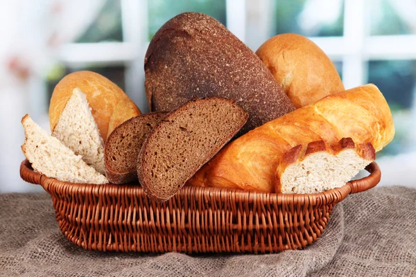 Pão fresco na cesta na mesa de madeira no fundo da janela — Fotografia de Stock
