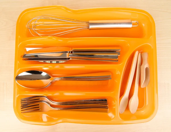 Orange plastic cutlery tray with checked cutlery and wooden spoons on wooden table — Stock Photo, Image