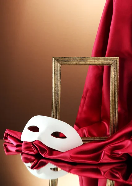 White mask, empty frame and golden silk fabric, on red background — Stock Photo, Image