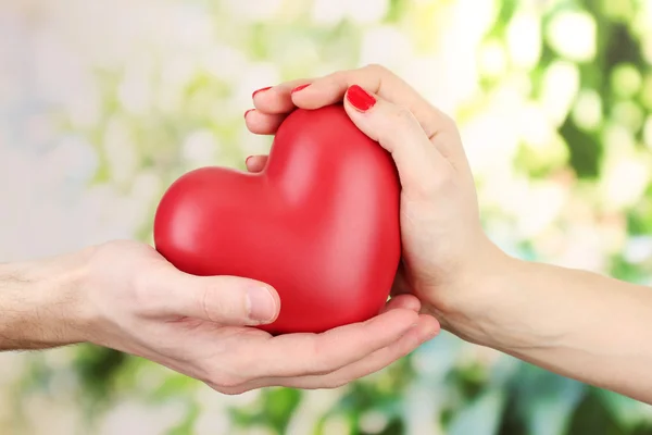 Kadın ve adam ellerini, yeşil zemin üzerine kırmızı kalp — Stok fotoğraf