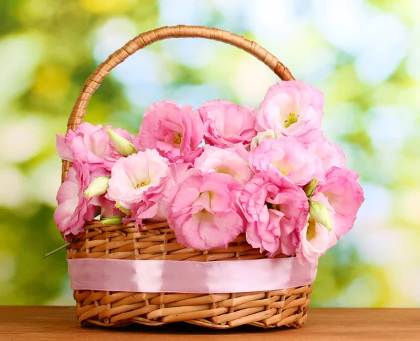 Bouquet of eustoma flowers in basket, on wooden table, on green background — Stock Photo, Image