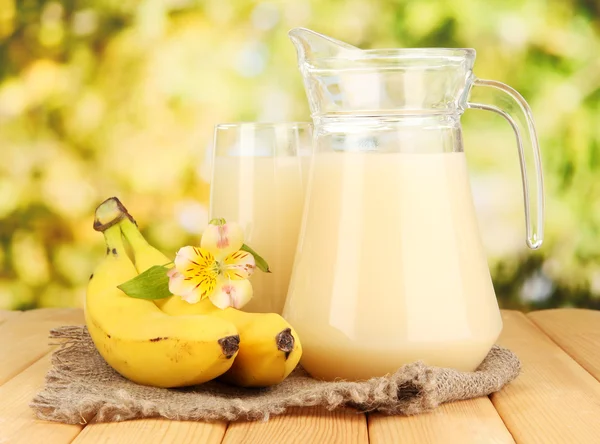 Copo cheio e jarro de suco de banana e bananas na mesa de madeira ao ar livre — Fotografia de Stock