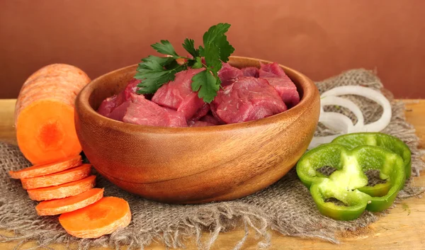 Carne de res cruda en tazón con verduras sobre mesa de madera sobre fondo marrón — Foto de Stock