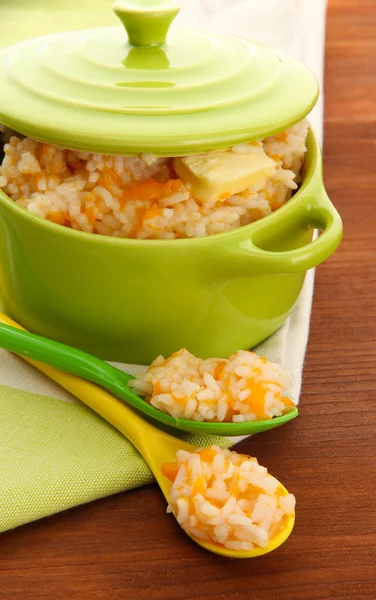 Taste rice porridge with pumpkin in saucepan on wooden background — Stock Photo, Image