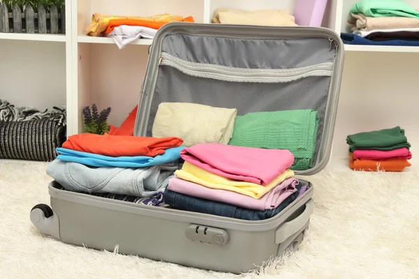 Open grey suitcase with clothing in room — Stock Photo, Image