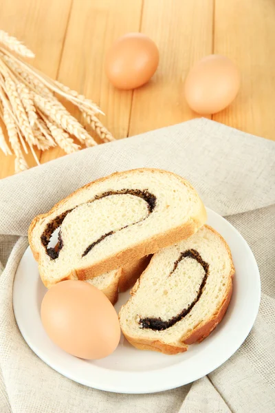Loaf with poppy seeds on color plate, on wooden background — Stock Photo, Image