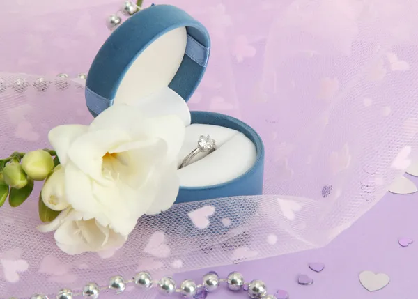 Vacker låda med vigselring och blomma på lila bakgrund — Stockfoto