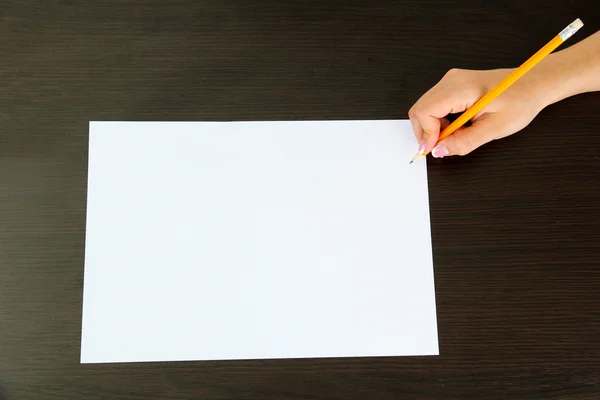 Рука с карандашом на белой бумаге, на деревянном фоне — стоковое фото