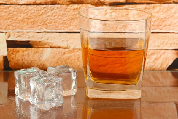 Glass of whiskey and ice on brick wall background — Stock Photo, Image